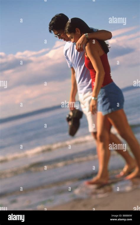 Young Couple Walking On Beach Man With Arm Around Womans Shoulder