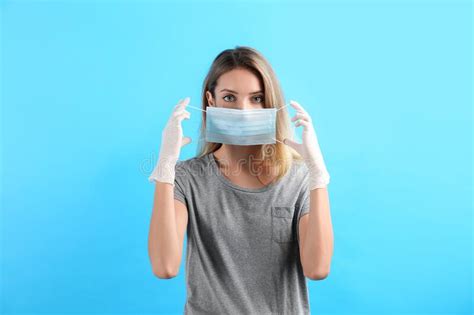 woman in medical gloves putting on protective face mask against light blue background stock