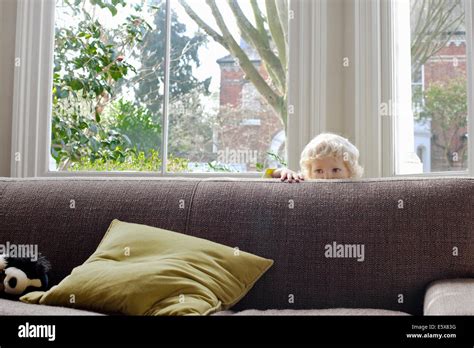 Portrait of cute male blond toddler hiding behind sofa Stock Photo - Alamy