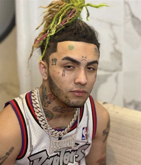 A Man With Tattoos And Piercings On His Face Sitting In Front Of A Couch