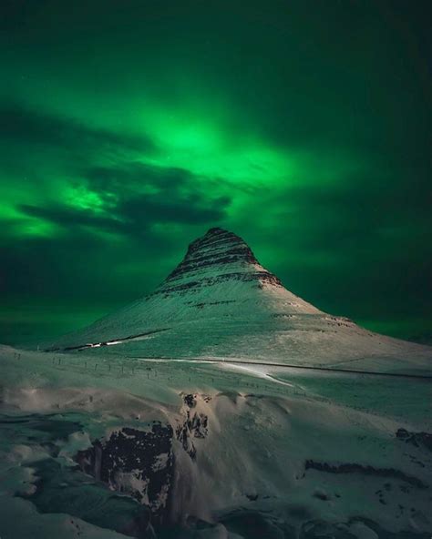A Green And White Aurora Bore Over A Snow Covered Mountain In The Night