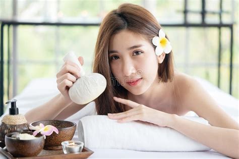asian woman lying down on massage bed holding herbal compress ball waiting for body care