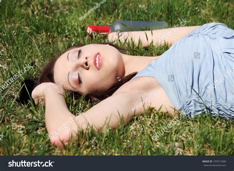 Drunk Young Woman Is Sleeping On The Grass Next To Bottle Of Alcohol In