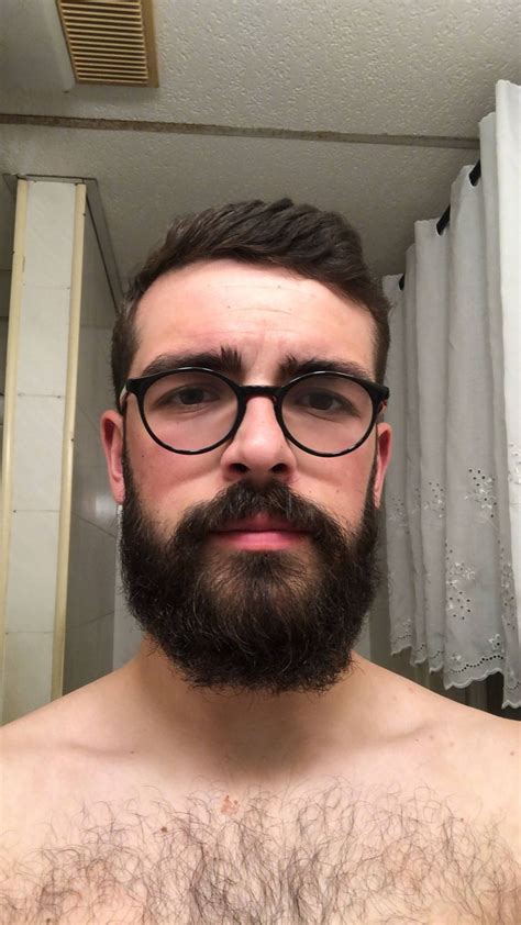 a man with glasses and a beard is taking a selfie in the bathroom mirror