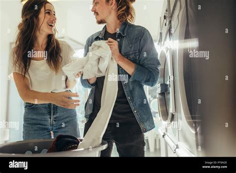 Happy Couple Having Fun Doing Laundry Together Couple Standing In A Laundry Room Putting