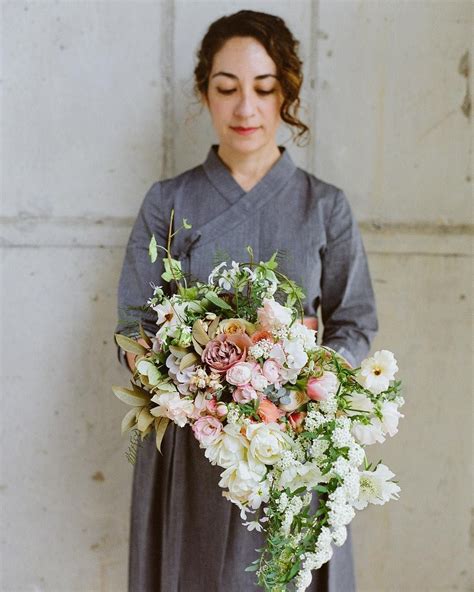 A Woman Holding A Bouquet Of Flowers In Front Of A White Wall With