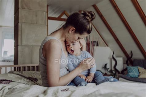 Mother Cuddling Tired Baby Son In Bed — Together Care Stock Photo