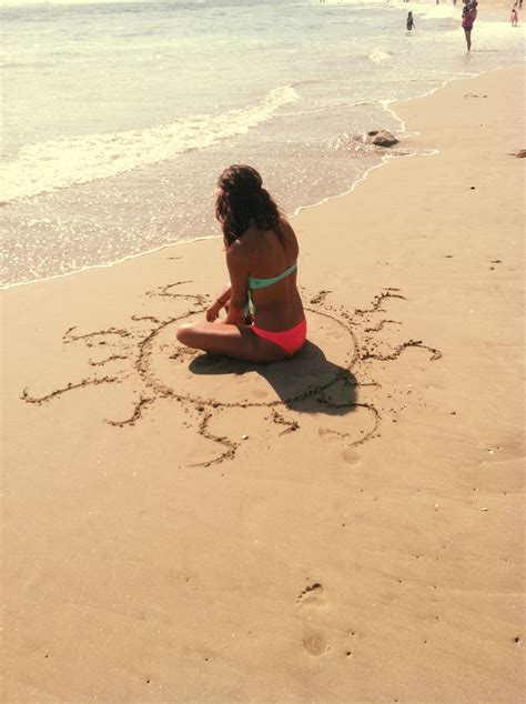 A Woman Sitting On Top Of A Beach Next To The Ocean Drawing In The Sand