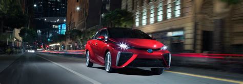 Red 2018 Toyota Mirai Driving With Headlights On Through City Street At