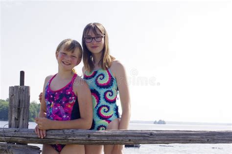 Pair Of Teen Girls Standing At Wooden Rail Rustic Fence In Summer Bathing Suits On Sunny Day