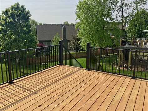 A Wooden Deck With Black Iron Railings And Trees In The Back Ground On