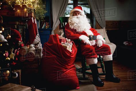 Portrait Of Santa Claus Sitting In Chair With Sack Full Of Presents