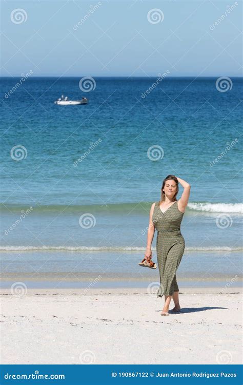 Mujer Rubia De Mediana Edad Con Un Vestido Verde Caminando Descalzo En La Playa Foto De Archivo