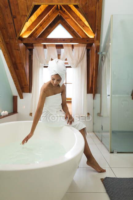 Mixed Race Woman In Bathroom Running A Bath Sitting On The Edge Of Tub