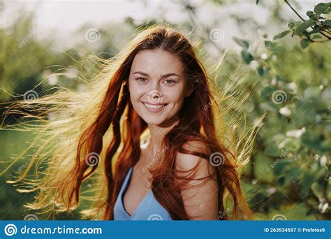 Beautiful Woman With Long Red Hair Near A Tree In The Summer Sun In The