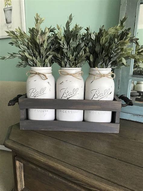 Three Mason Jars Filled With Greenery Sitting On Top Of A Wooden Table