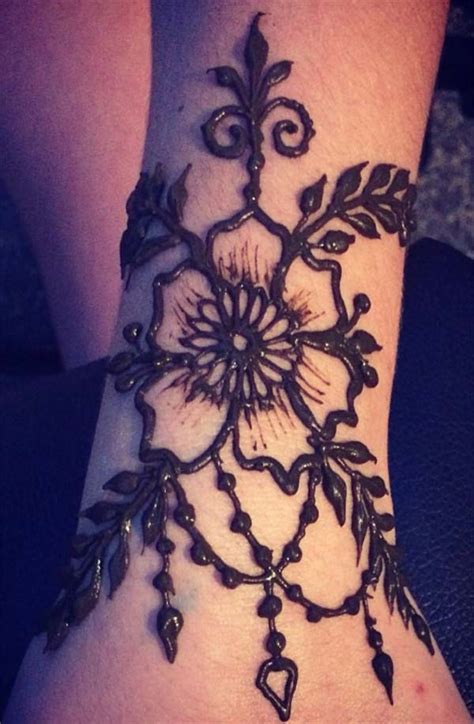 This black henna tattoo, rendered on the wearer's wrist and handm, features a floral inspired design that descends down the wearer's middle finger a crescent moon design embellished with dangling beads is rendered on the wearer's left hand in this henna tattoo. Henna Mehndi tattoo designs idea for wrist - Tattoos Art Ideas