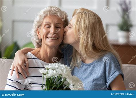 Abuela Feliz Recibiendo Un Beso Tierno Y Flores De Su Nieta Adulta Foto