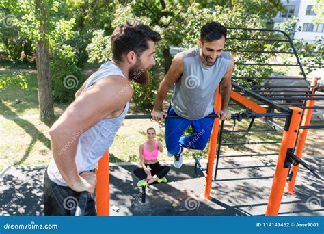 Two Muscular Young Men Doing Bodyweight Exercises In Fitness Park Stock