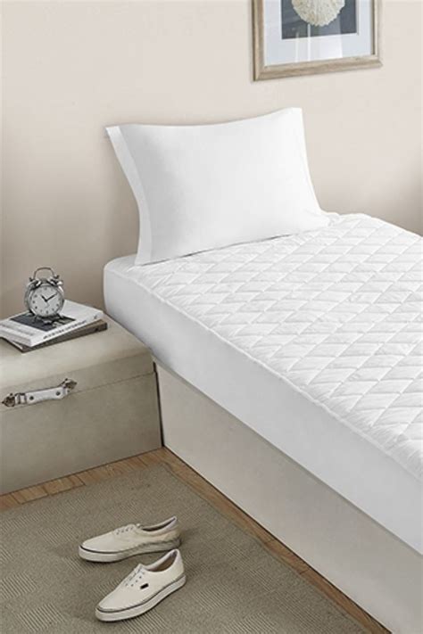 A Bed With White Sheets And Slippers On The Floor Next To A Wall