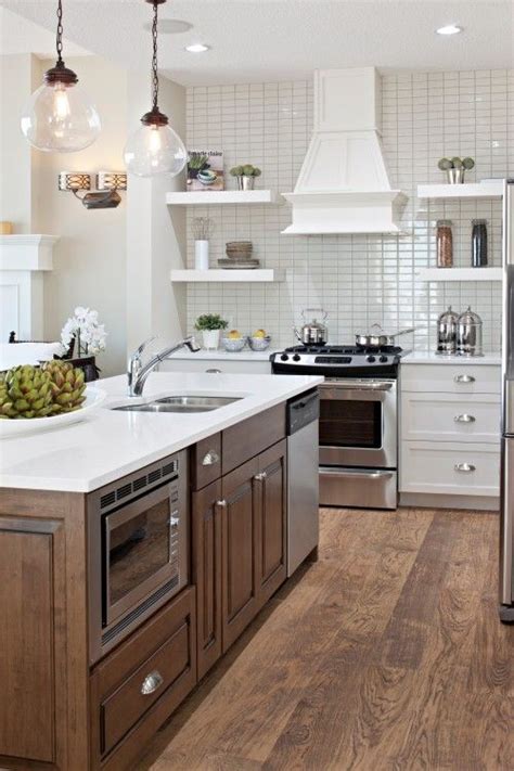 White and brown kitchen design features hudson valley lambert brass and white pendants over a a dark brown kitchen island with a white quartz waterfall edge countertop with gray fabric stools, white cabinetry with brown honeycomb tiles, a stainless steel hood over cooktop, and a sink with a gooseneck faucet. I like the lights over the island and the dark wood island ...