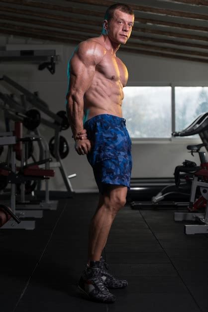 Homem bonito em pé forte na academia e flexionando os músculos muscular atlético fisiculturista