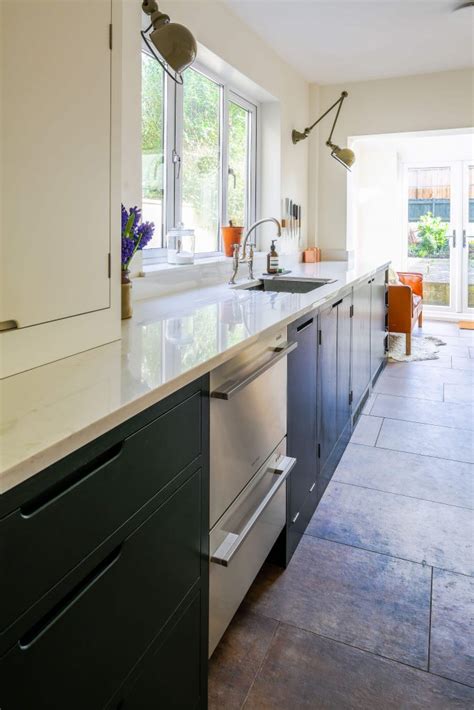Classic white cabinets reflect light from the base cabinets wear a muted green paint. Green Industrial Style Galley Kitchen - Sustainable Kitchens