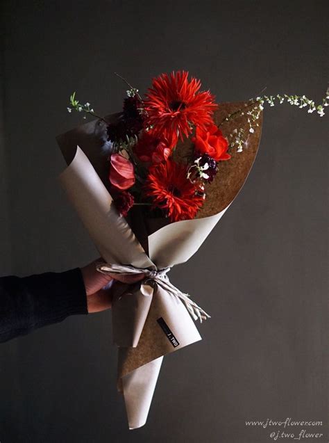 A Person Holding A Bouquet Of Flowers Wrapped In Brown Paper And Tied