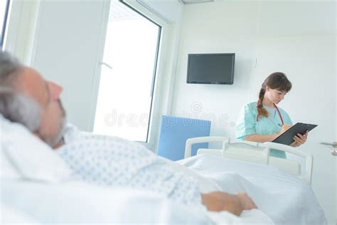 Doctor Taking Notes From Man Patient Lying In Hospital Bed Stock Image