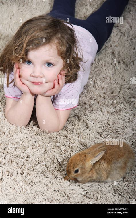 Little Girl Playing With A Little Rabbit On The Carpet In The