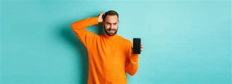 Free Photo Confused Guy Scartching Head And Showing Smartphone Screen