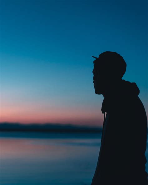 Silhouette Of Man Standing On Shore At Sunset · Free Stock Photo