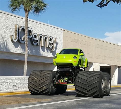 A Green Monster Truck Parked In Front Of A Jc S Store With Large Tires