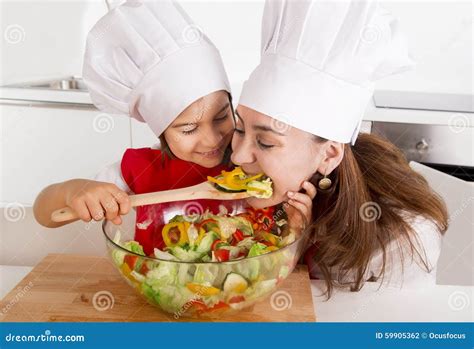 Happy Mother And Little Daughter At Home Kitchen Preparing Salad In Apron And Cook Hat Stock