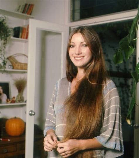 A Woman With Long Brown Hair Standing In Front Of A Door And Smiling At