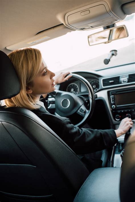 Blonde Young Woman Holding Gear Shift Handle While Sitting In Car Free