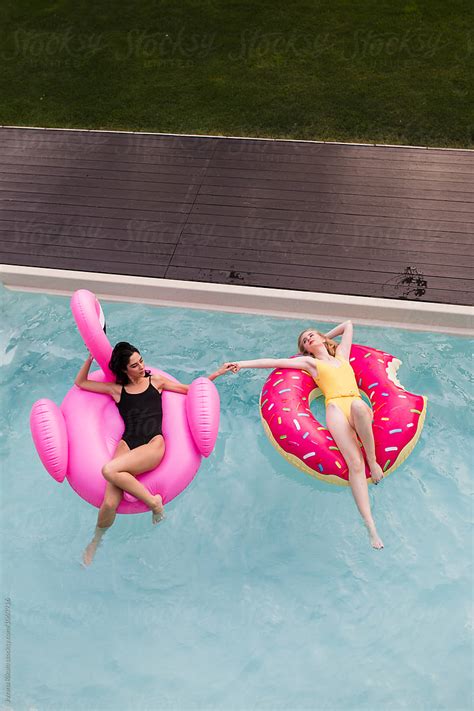 Two Female Friends Floating On A Big Flamingo In The Swimming Pool Del Colaborador De Stocksy