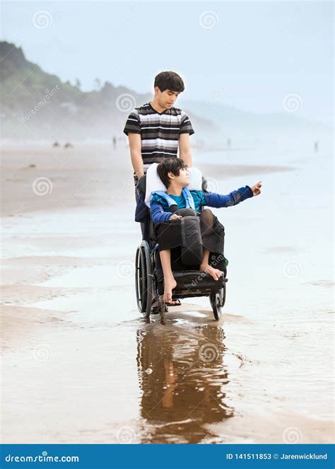 Young Man Pushing Disabled Brother In Wheelchair On Beach Stock Image