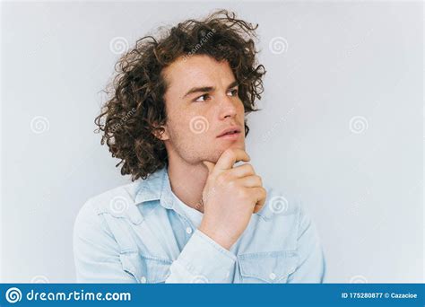 Studio Shot Of Handsome Pensive Male Model With Curly Hair Wears Blue Shirt Looking Up
