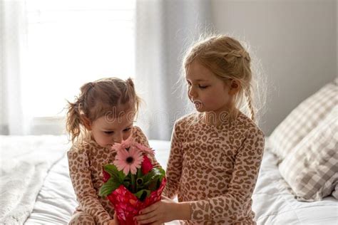 Two Little Girls In Matching Pajamas Holding Flowers To Surprise Mom