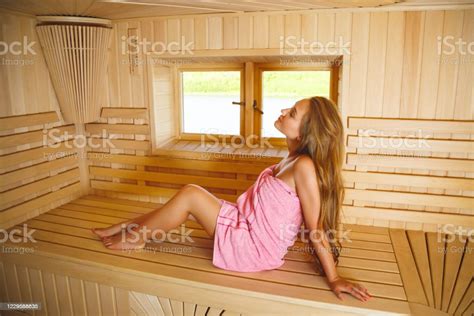 The Lovely Girl In A Pink Towel Sits In A Sauna On A Bench And Enjoys