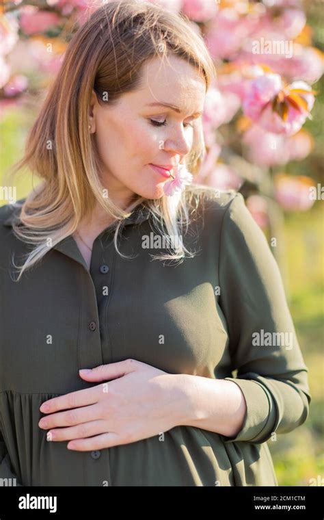 freckled blonde pregnant woman in the park at spring with sakura trees shallow depth of field