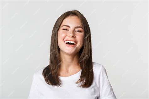 Крупный план счастливой девушки брюнетки в белой футболке беззаботно смеясь и улыбаясь в камеру