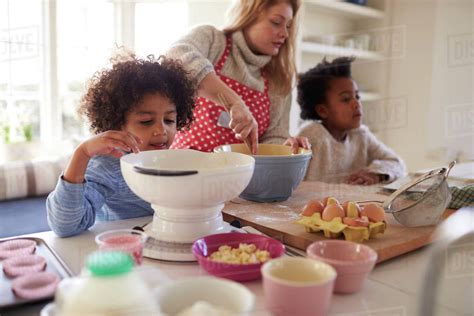 Mother Baking Cake With Children In Kitchen At Home Stock Photo
