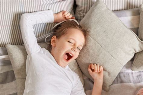 Sleepy Little Girl Yawning In The Morning While Lying In Bed On Pillows