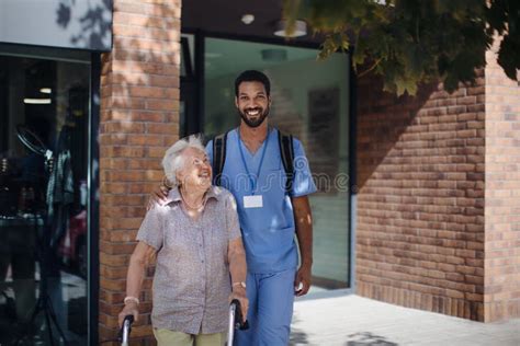 Caregiver Walking With Senior Woman Client In Front Of Nurishing Home