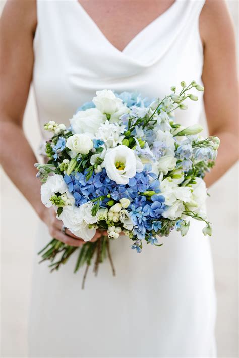 A Woman In A White Dress Holding A Bouquet Of Blue And White Flowers On