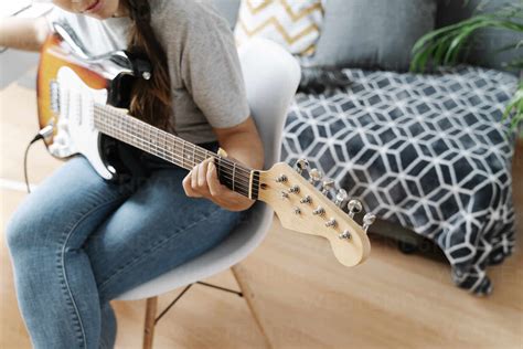Woman Playing Electric Guitar While Sitting On Chair At Home Stock Photo