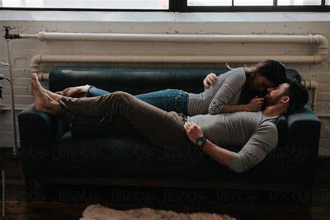 Attractive Young Interracial Couple Cuddling On Couch In Trendy Loft Apartment By Stocksy