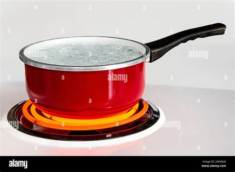 horizontal shot of a red pan of boiling water on top of a stove with the burner turned to high
